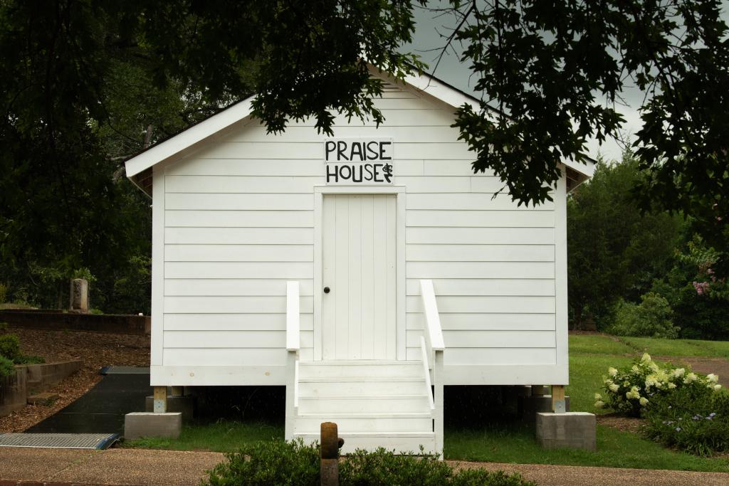 Small white house with sign reading "praise house" in black lettering above front door.
