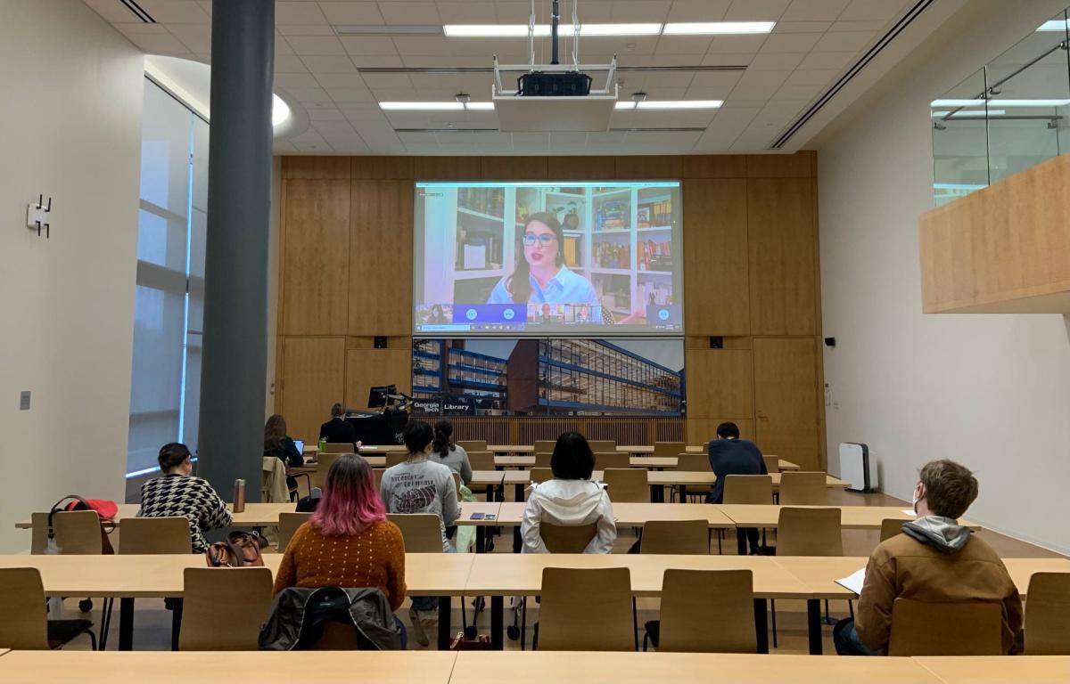 Meagan Martz on the projector screen with in-person attendees seated in the Price Gilbert Library Scholars Event Theater on March 16, 2022.