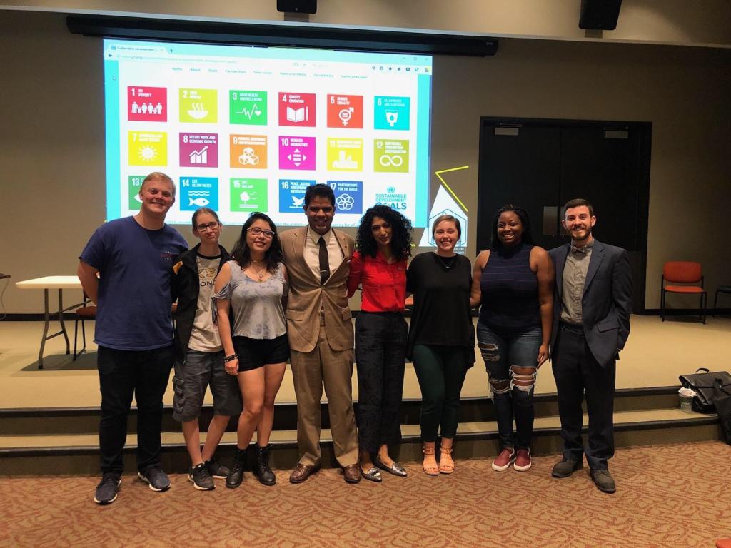 Students stand in front of a digital display of the Sustainable Development Goals.