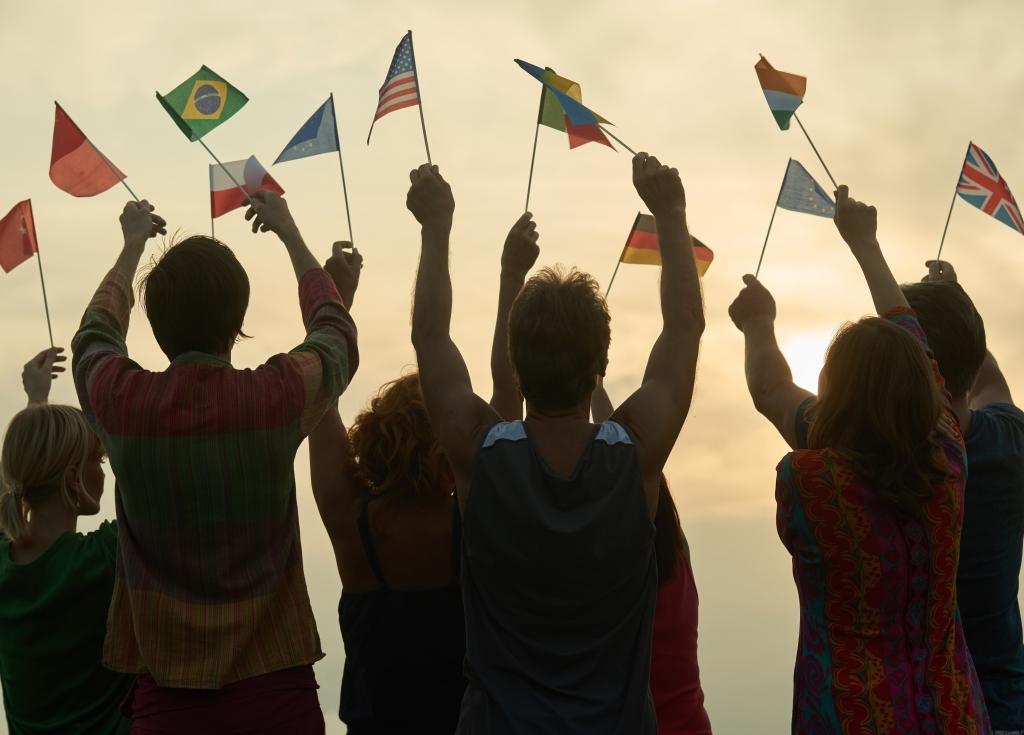 Silhouette of students holding multiple international flags at sunset.
